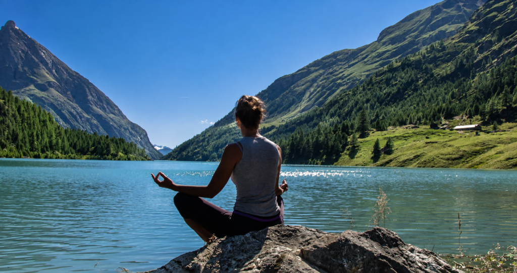 Persona in meditazione davanti a un lago alpino